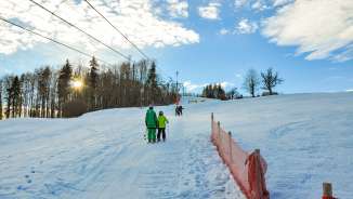 Skifahrerinnen und Skifahrer an einem Schlepplift mit Sonnenschein